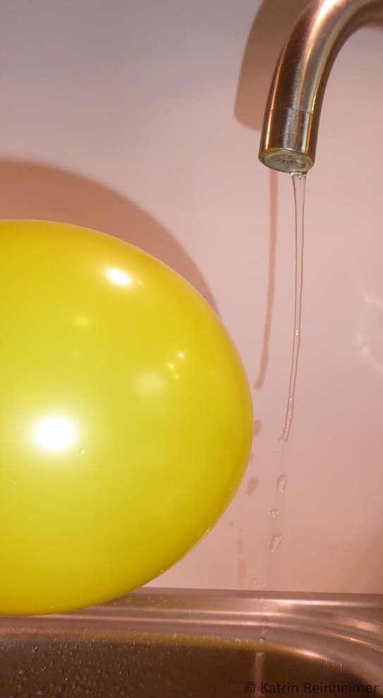 Der Wasserstrahl wird von einem elektrostatisch aufgeladenen Luftballon angezogen.