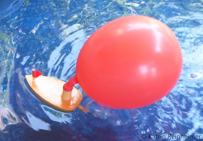 Der Luftballon an einem Holzboot. Die ausströmende Luft treibt das Boot an.