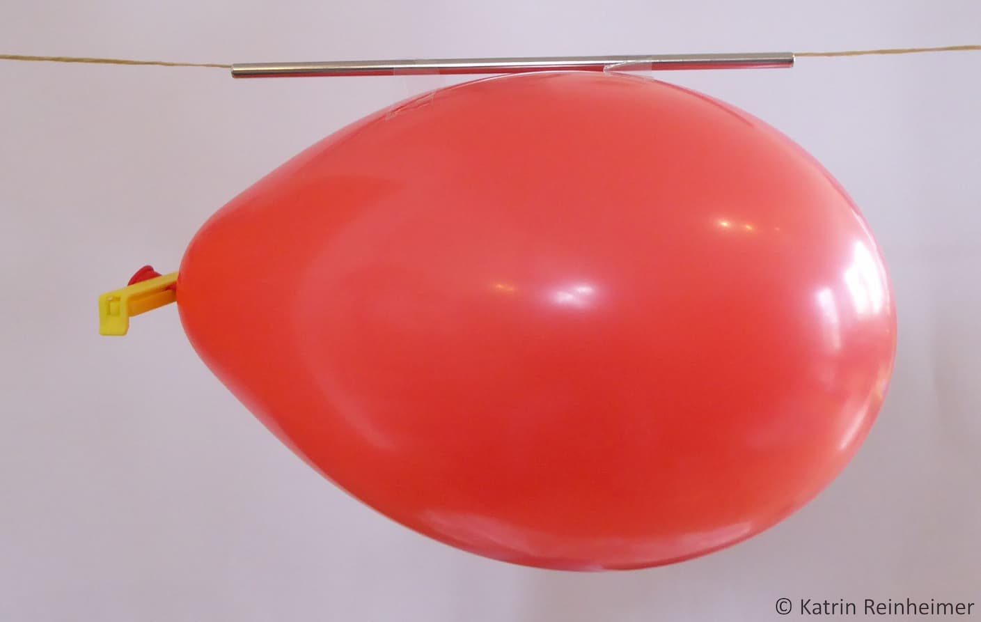 Der Luftballon hängt an einem Trinkhalm, verschlossen mit einem Verschlussclip.